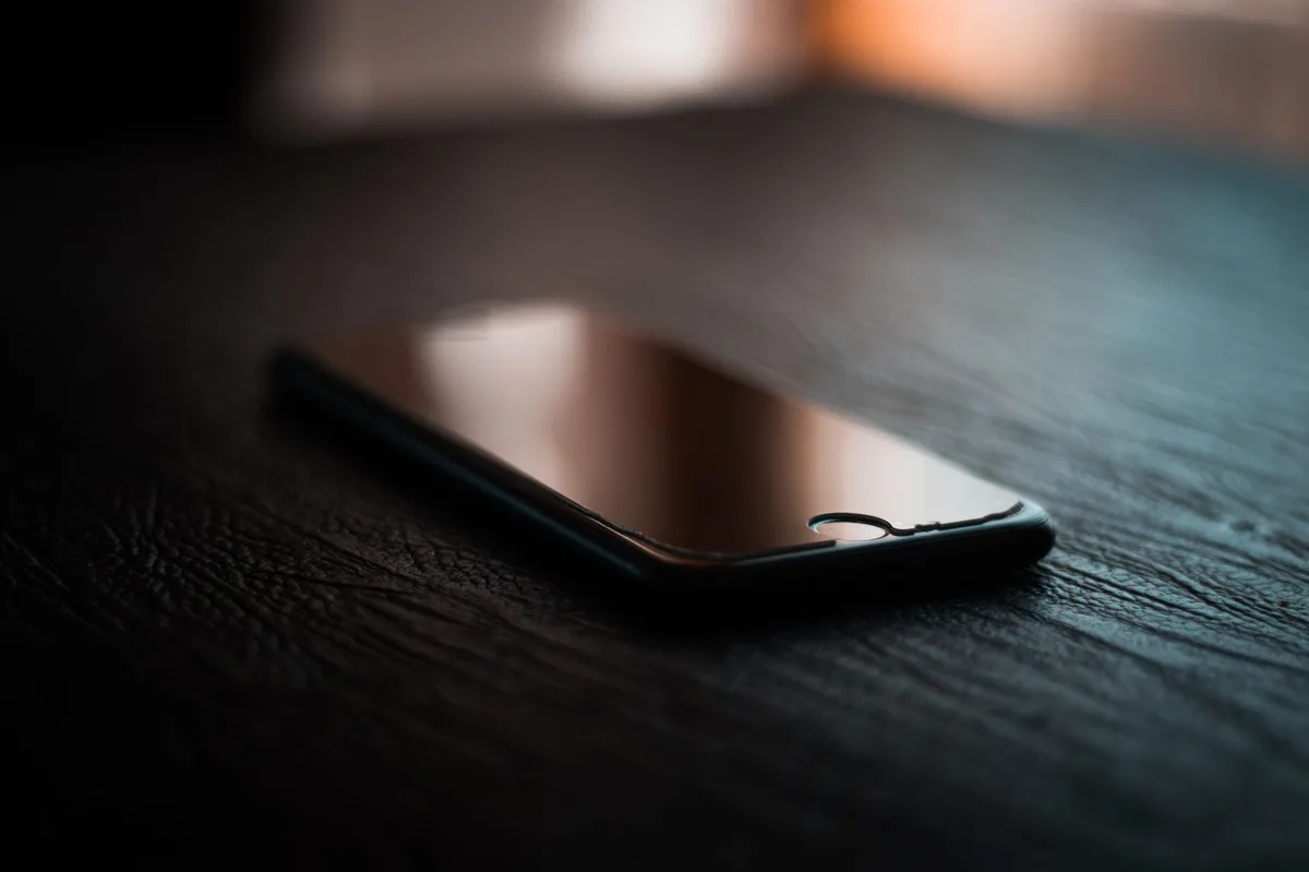 Mặt lưng một chiếc điện thoại thông minh đặt trên mặt bàn tối màu, không thấy nhãn hiệu